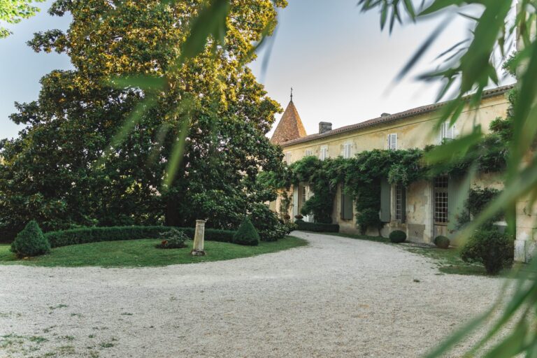Façade en pierre du Château de Puyrigaud, à Léoville, avec sa tour, sa vigne vierge et sa cour en gravier