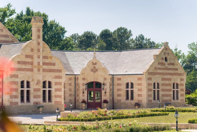 Bâtiment en pierre et briques du Domaine de Grenade, à Saint-Selve, avec ses parterres de fleurs et ses grands arbres