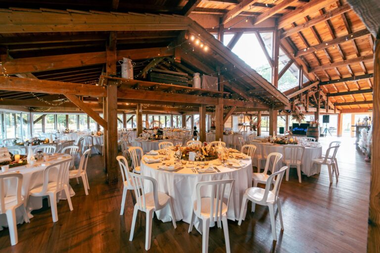 Grande salle en bois de La Ferme d'En Chon, à Biscarrosse, avec ses poutres apparentes et ses tables rondes dressées