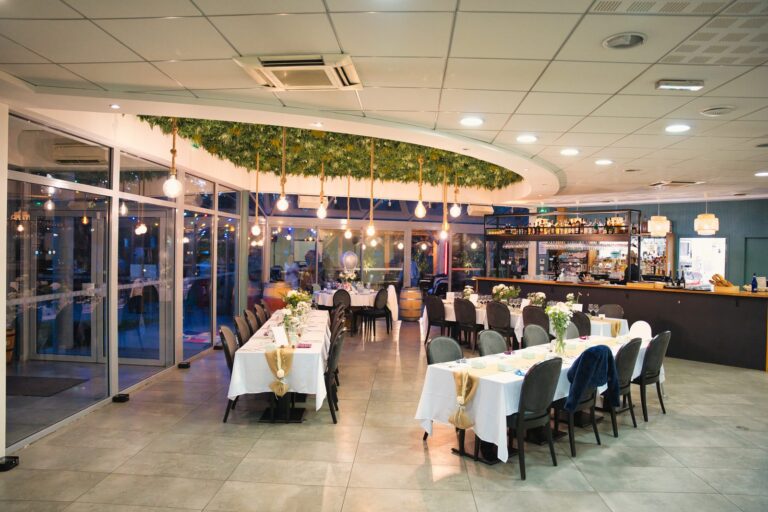Salle vitrée du Le 1902 (Brasserie 1902) à Ludon-Médoc, avec ses tables dressées et son bar au fond