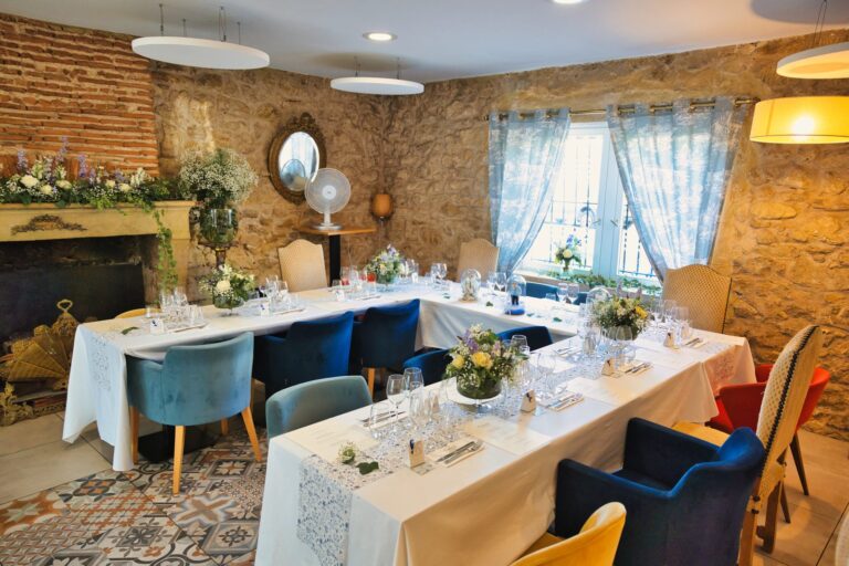 Salle de réception du Grangousier, à Langon, avec ses murs en pierre, sa cheminée fleurie et la table en U dressée