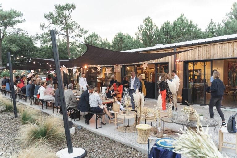 Terrasse et bâtiment en bois des Frères Nicoll's à Soulac-sur-Mer, sous les pins, avec des convives attablés