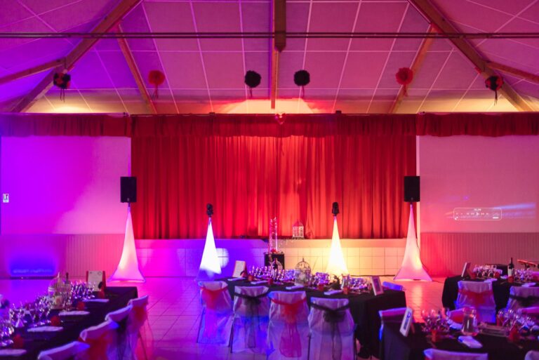 Salle polyvalente de Loupes aménagée pour le dîner de mariage, avec tables décorées et rideau rouge éclairé
