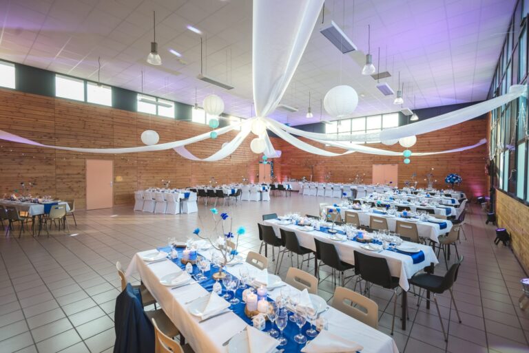Salle des fêtes de Lamothe en Haute-Loire décorée pour un mariage : tables dressées en bleu et blanc sous des voilages et lanternes.