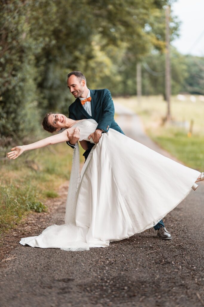 Sur un chemin bordé d'arbres, le marié penche la mariée en arrière, bras tendu, dans un grand pas de danse.