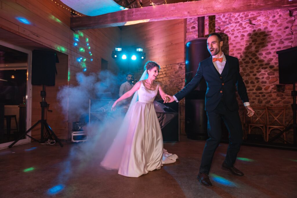 Les mariés ouvrent le bal sur la piste dans la fumée, la mariée en robe blanche et le marié en costume sombre se tenant par la main.