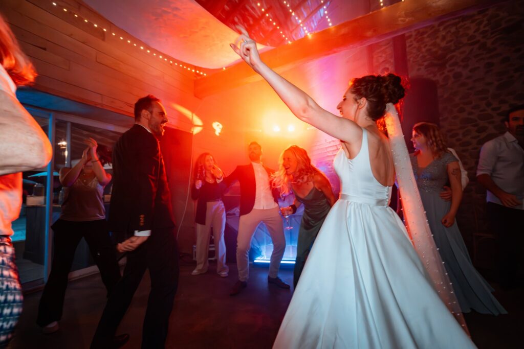 La mariée, un bras levé vers les projecteurs rouges et orange, danse sur la piste au milieu des invités.