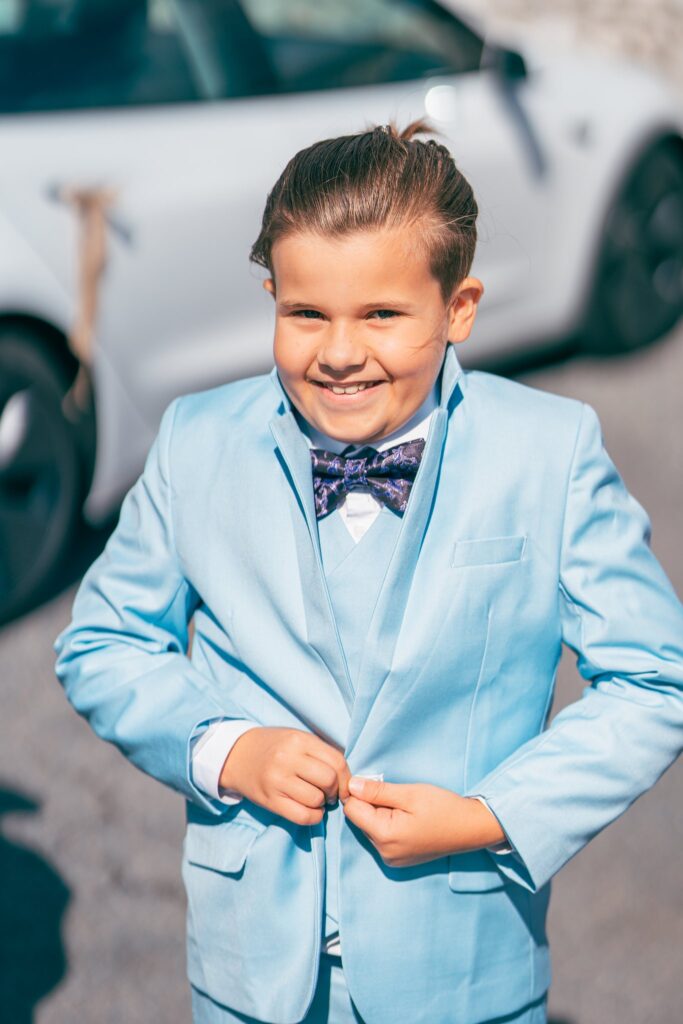 Un garçon en costume bleu ciel et nœud papillon sourit en boutonnant sa veste.