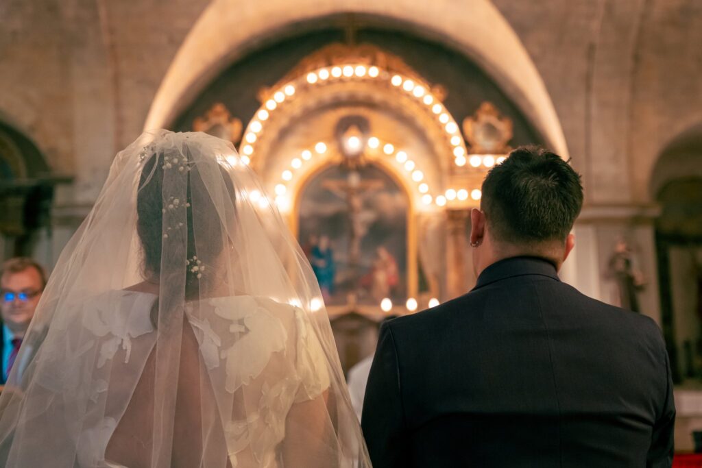 La mariée voilée, de dos, face au marié devant un autel éclairé de guirlandes lumineuses.