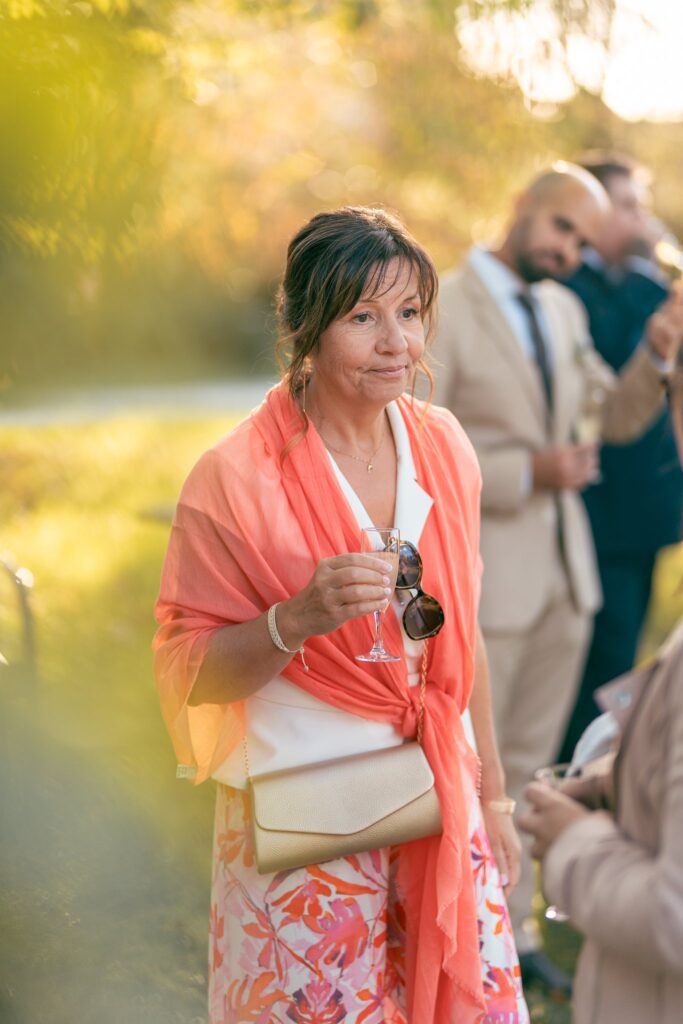 Une femme au foulard orange tient ses lunettes de soleil dans la lumière du soir.