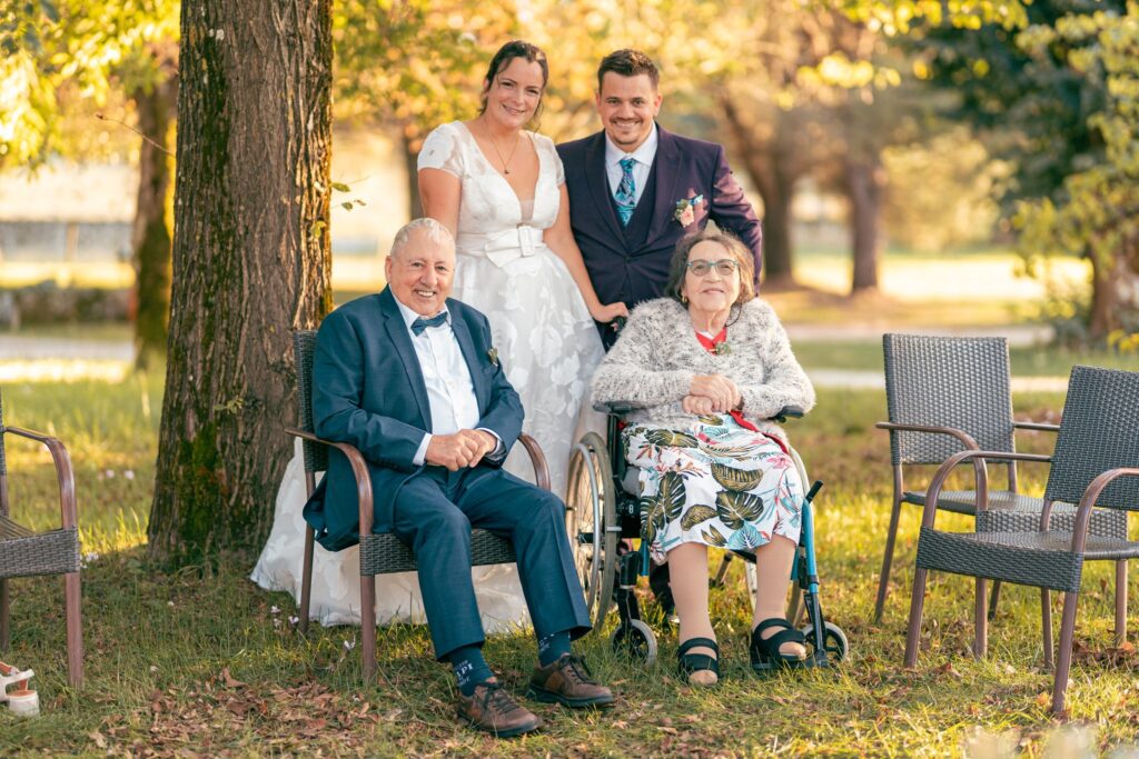 Les mariés posent dans un parc avec un homme âgé et une femme âgée en fauteuil roulant, assis devant eux.
