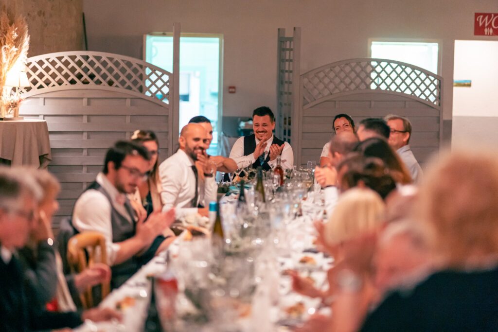 Des convives rient autour d'une longue table dressée pour le repas.