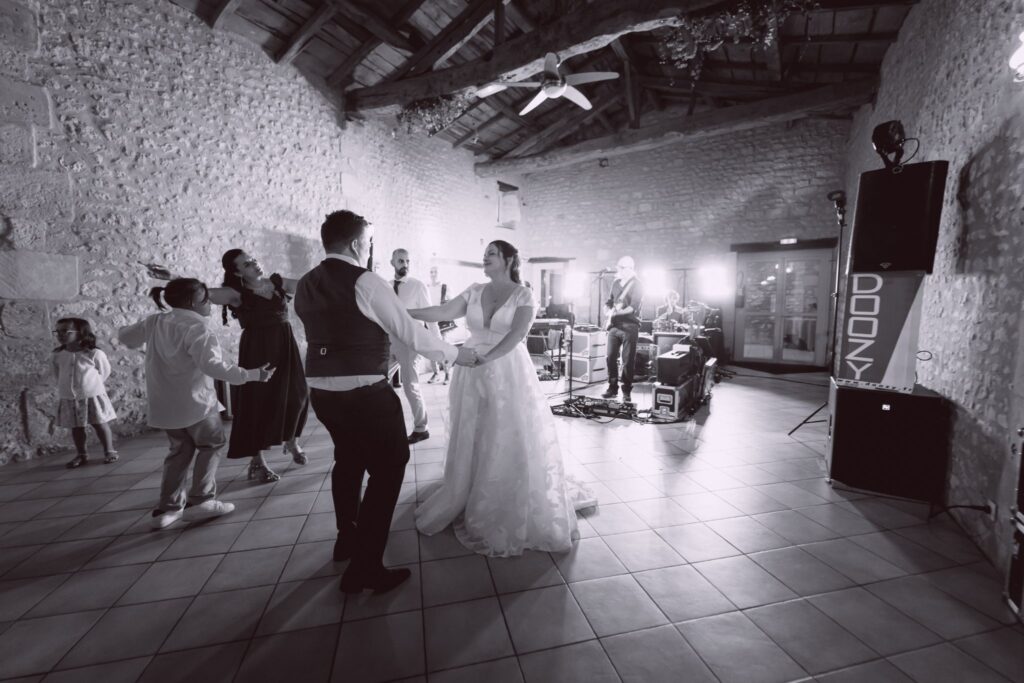 En noir et blanc, le couple danse dans une grange en pierre avec des invités.