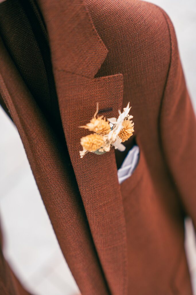 Gros plan sur une boutonnière de fleurs séchées épinglée au revers d'une veste couleur rouille.