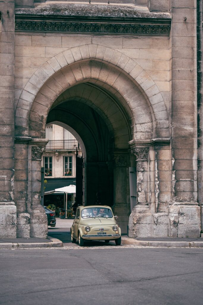 Une petite voiture ancienne garée sous une voûte en pierre, dans une rue d'Angoulême.