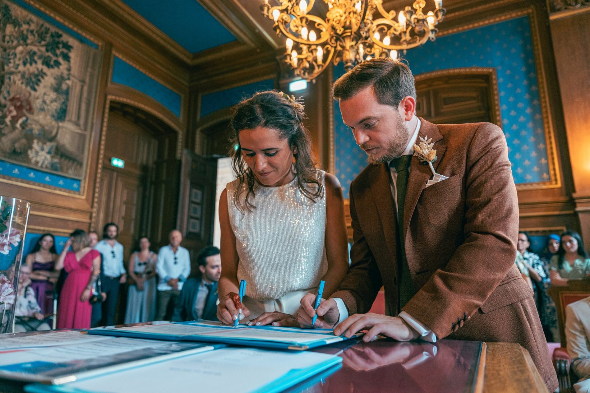 La mariée et le marié signent le registre, penchés côte à côte sur la table de la salle des mariages.
