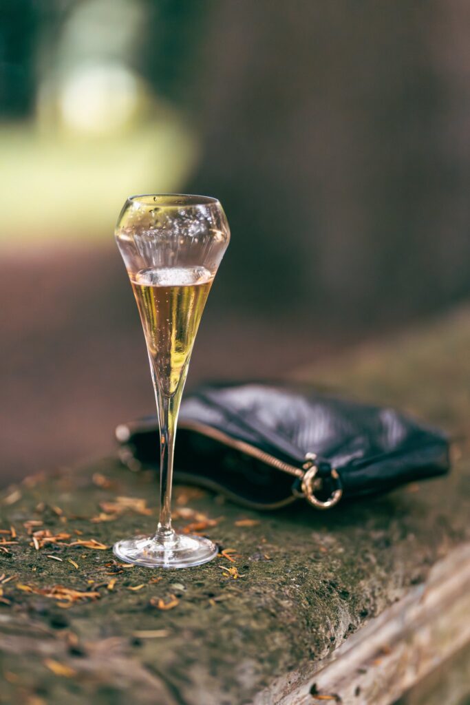 Une flûte de champagne posée sur une pierre, à côté d'une pochette noire, dans la lumière dorée du soir.