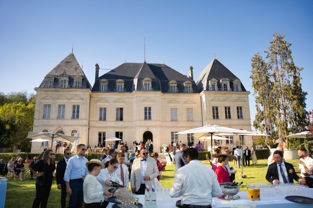 Au château, des invités se retrouvent sur la pelouse et sous les parasols pour le vin d'honneur.