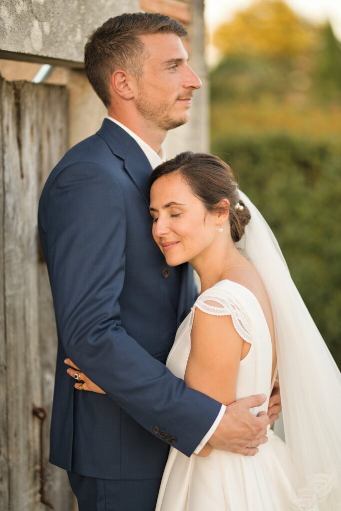 Le marié serre la mariée contre lui, adossés à une porte en bois, la mariée les yeux fermés.