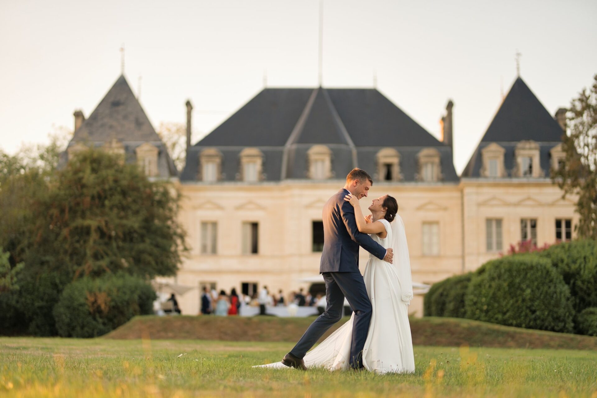 Les mariés s'embrassent en dansant sur l'herbe, le château à l'arrière-plan sous la lumière du soir.