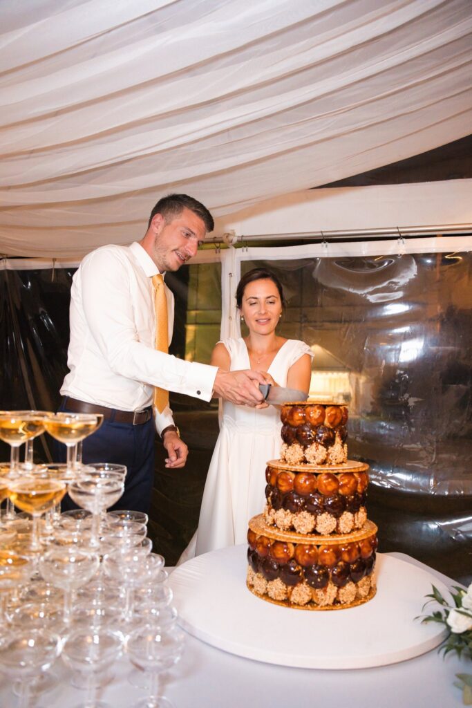 Les mariés découpent une pièce montée de choux à côté d'une pyramide de coupes de champagne.