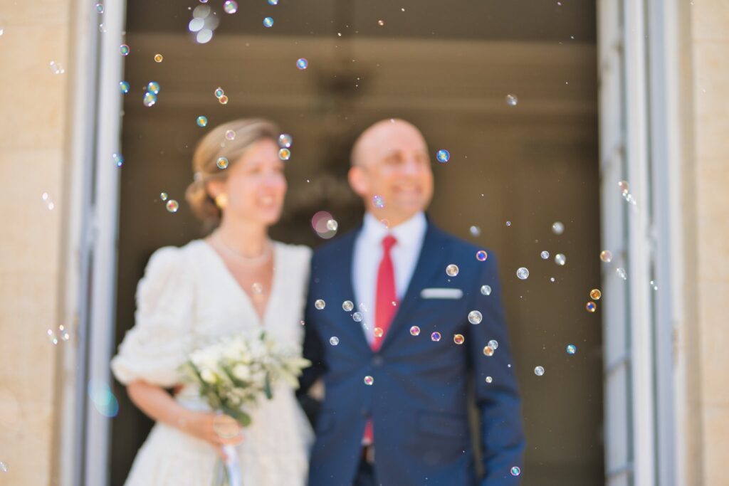 Le couple sur le seuil de la mairie, un bouquet blanc à la main, au milieu de bulles de savon.
