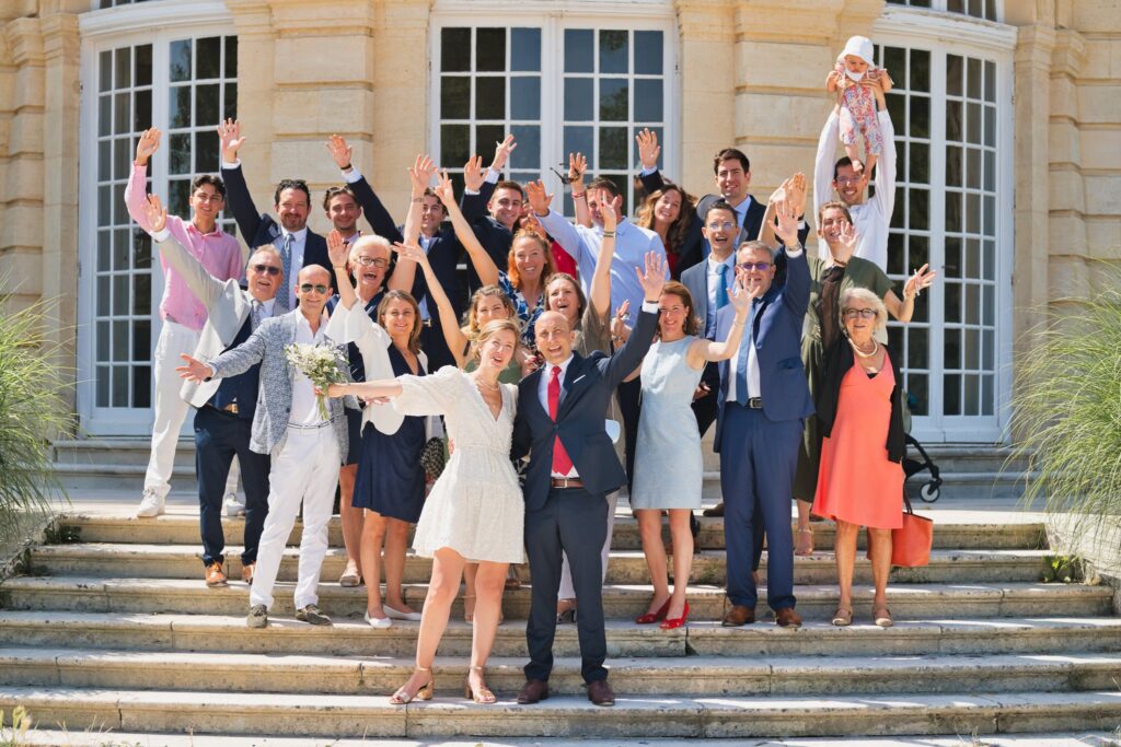 Les invités bras levés, posant avec les mariés sur les marches devant la façade de la mairie.