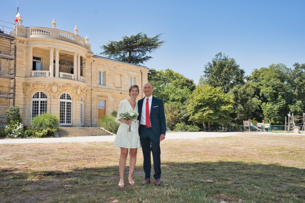 Les mariés côte à côte sur la pelouse, devant le bâtiment de la mairie et ses grands arbres.