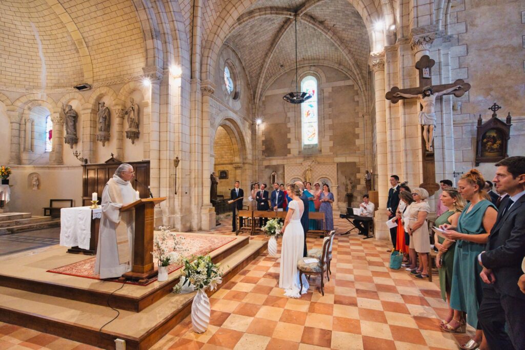 Vue large de la nef en pierre de l'église, avec le prêtre à l'autel et les invités debout.