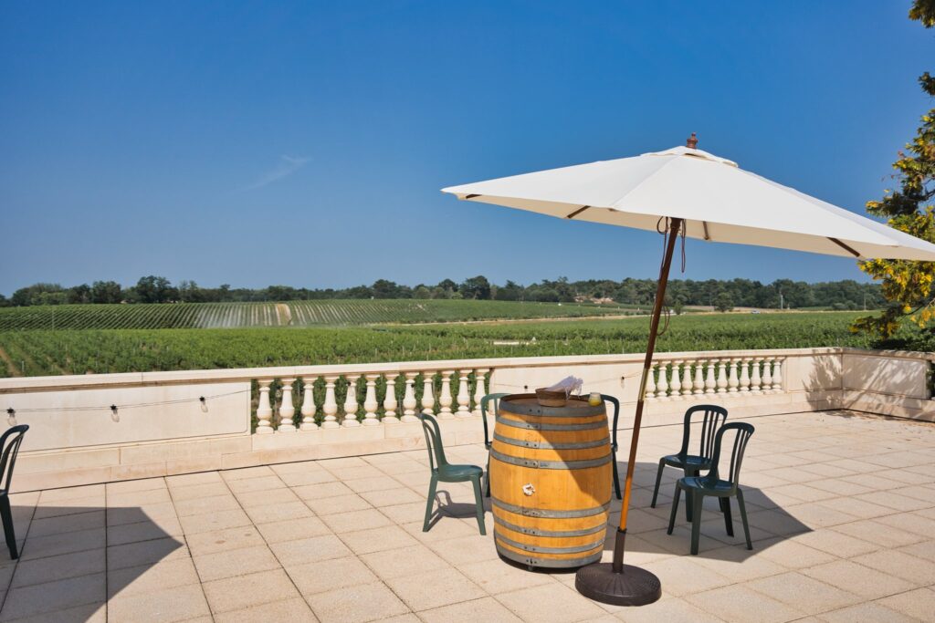 Une terrasse dallée avec un parasol blanc, un tonneau et une balustrade face aux vignes.