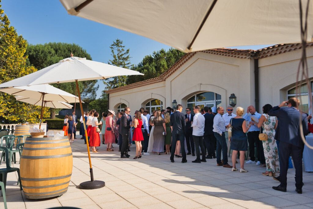 Des invités debout sur la terrasse sous les parasols, autour d'un tonneau, pendant le vin d'honneur.