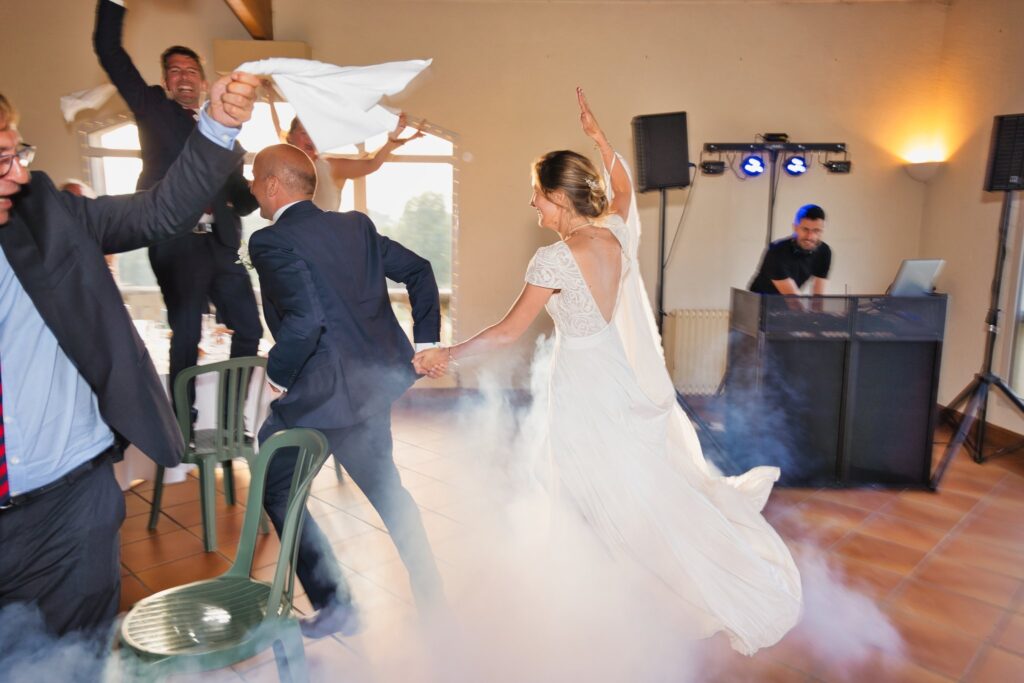 La mariée danse dans la fumée au sol de la salle, tandis que des invités agitent des serviettes blanches.