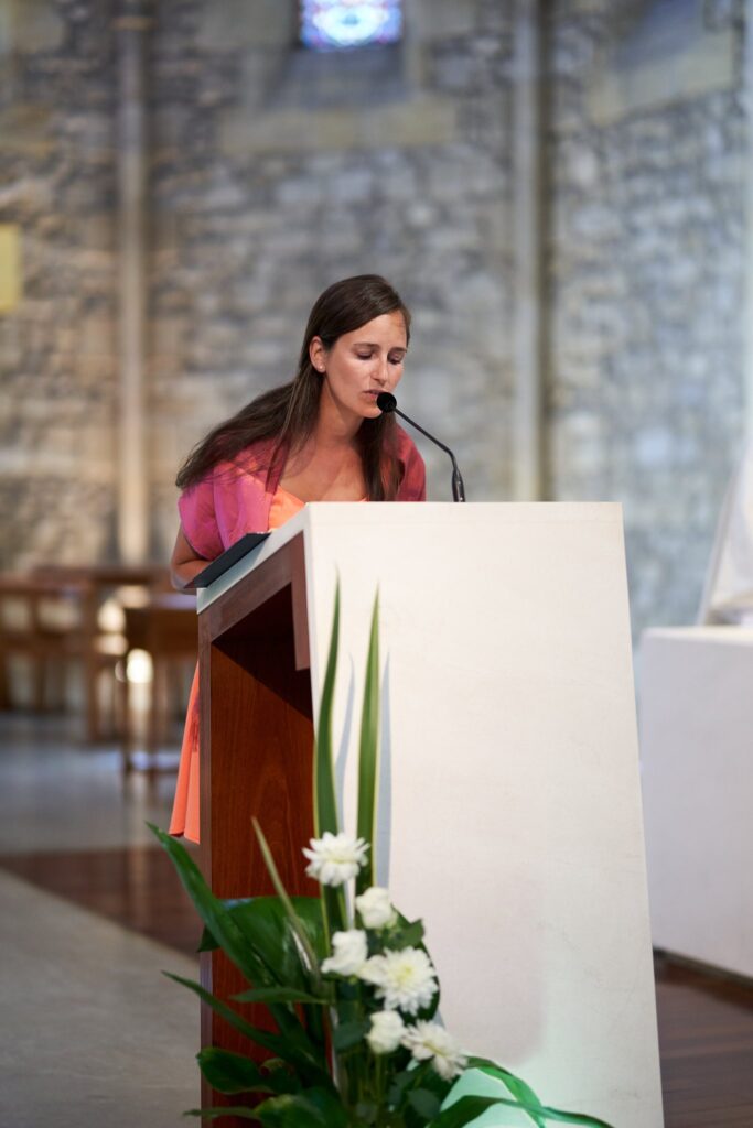 Une jeune femme lit un texte au micro, à un pupitre orné de fleurs blanches, dans l'église.