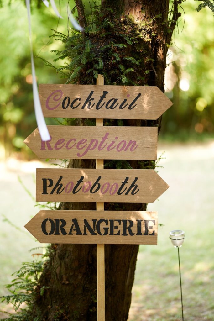 Panneau en bois indiquant Cocktail, Réception, Photobooth et Orangerie, fixé à un arbre.