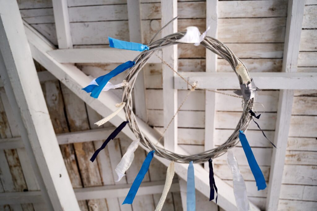 Couronne de brindilles ornée de rubans bleus et blancs, suspendue sous une charpente en bois.