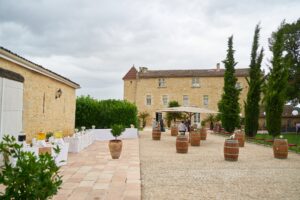 Cour pavée du Château Isabeau de Naujan avant le vin d'honneur : tonneaux, cyprès, oliviers en pot et façade en pierre blonde avec sa tourelle