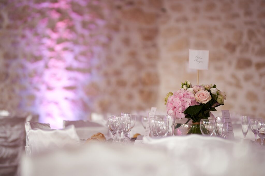 Table dressée avec un bouquet d'hortensias roses devant un mur de pierre éclairé, dans la salle de réception du château