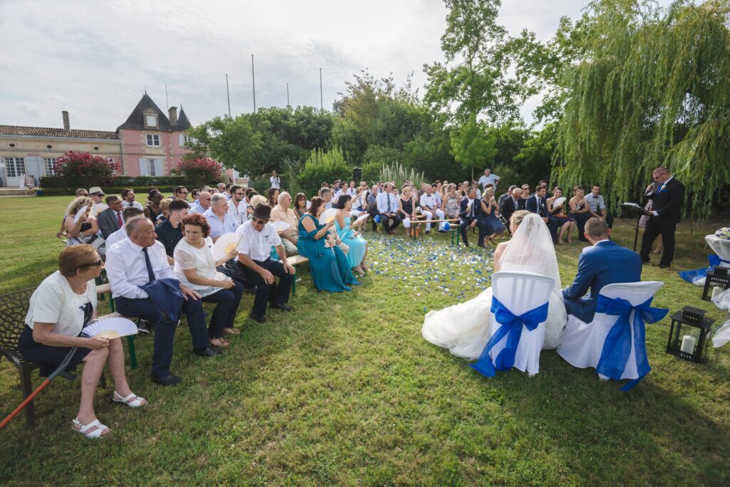 Cérémonie en plein air sur la pelouse devant le château rose, invités assis de part et d'autre d'une allée de pétales