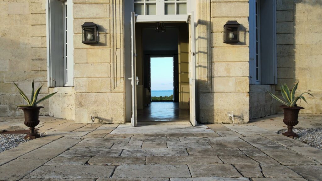 Porte ouverte du château donnant à travers le vestibule sur l'estuaire, deux urnes en métal de chaque côté