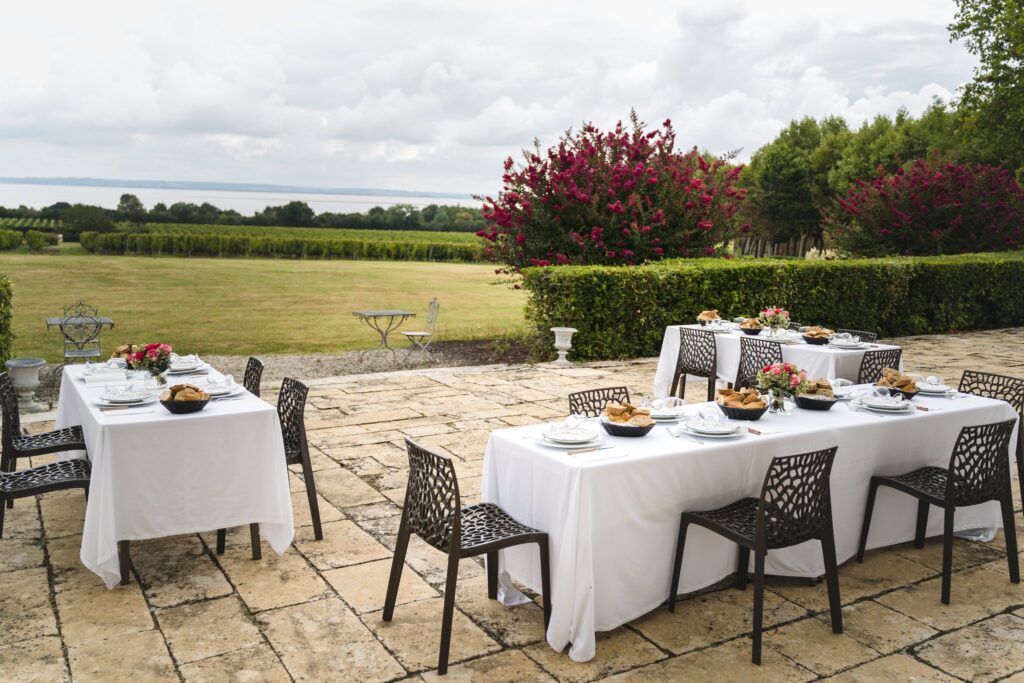 Tables dressées sur la terrasse de pierre, face à la pelouse, aux massifs rouges et à l'estuaire