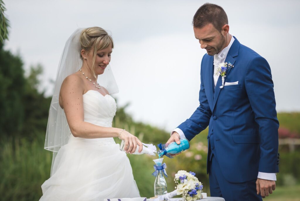 La mariée et le marié versent chacun du sable de couleur dans une même bouteille.