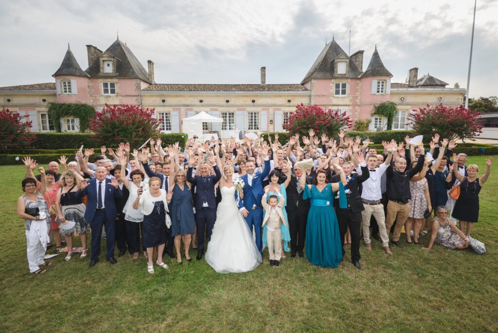 Photo de groupe sur la pelouse devant le château, les bras levés, avec les mariés au centre.