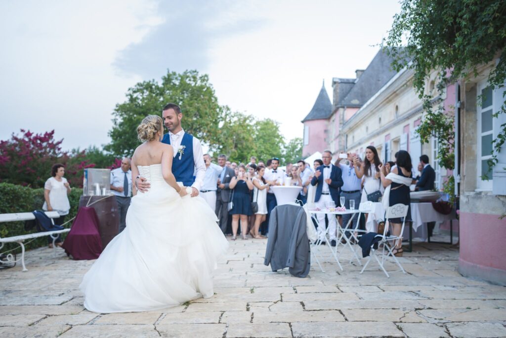 Les mariés dansent sur la terrasse de pierre, entourés d'invités debout, devant le château.