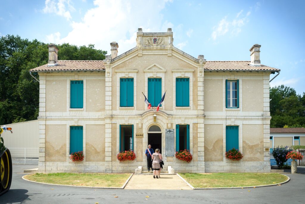 La façade d'une mairie en pierre claire aux volets turquoise, sous un ciel bleu.