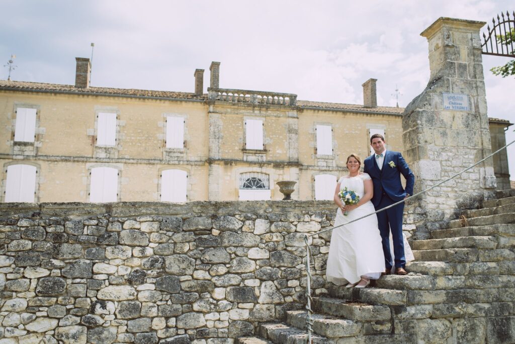 Les mariés sur un escalier de pierre devant la longue façade d'un château.