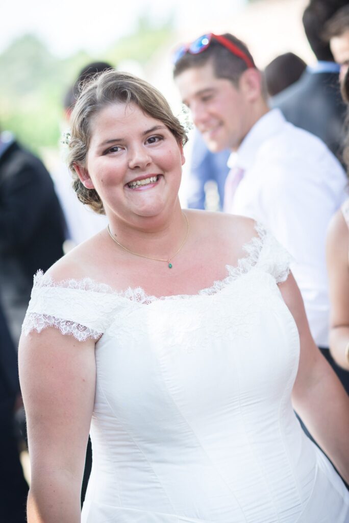 Portrait d'une mariée souriante en robe blanche à épaules dénudées, en extérieur.