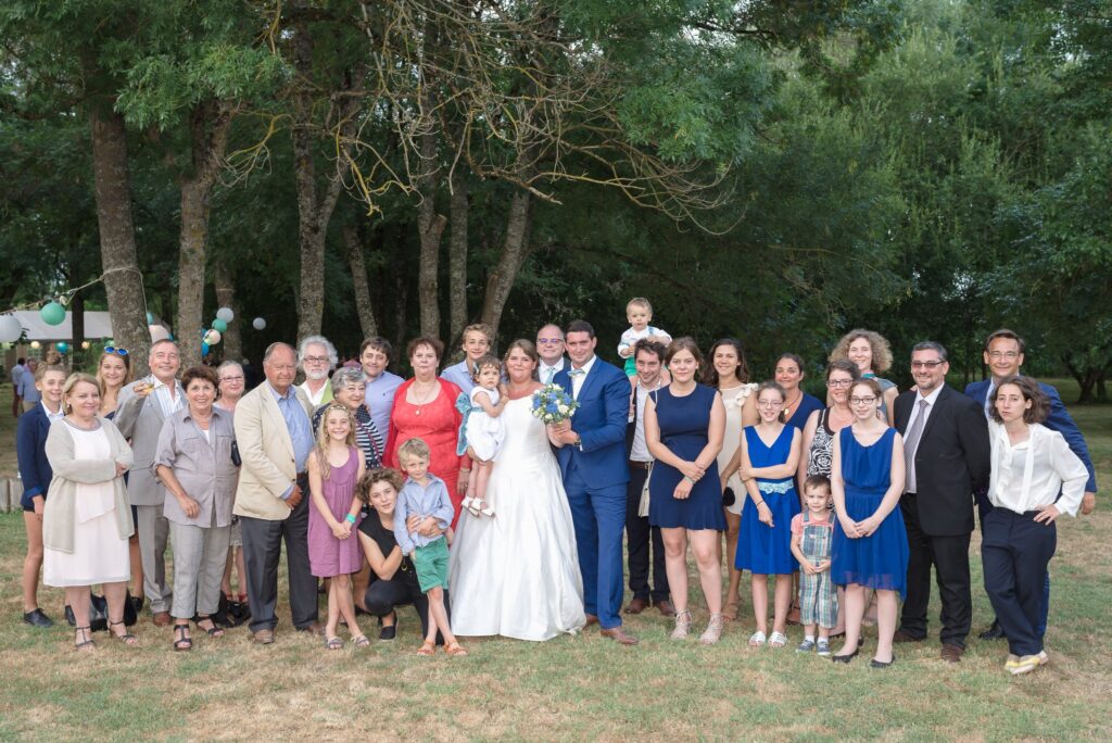 Photo de groupe des mariés et de leurs invités sous de grands arbres.