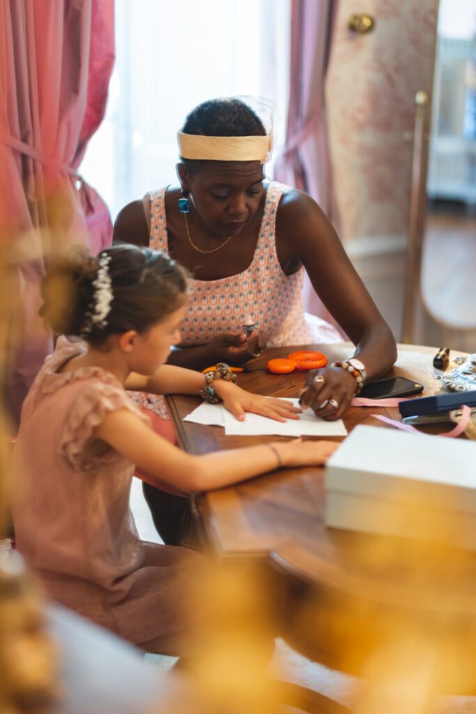 Une petite fille coiffée d'une fleur dans les cheveux et une femme travaillent ensemble à une table pendant les préparatifs.