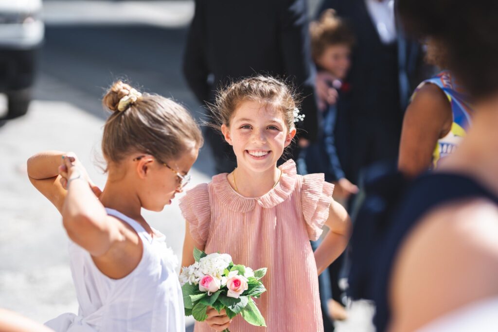 Deux petites filles en plein soleil dans la rue, l'une souriante tenant un bouquet de roses.