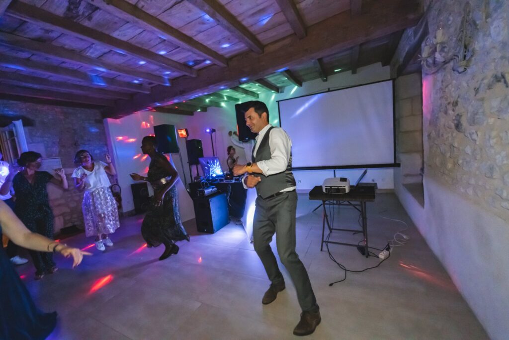 Un homme danse sur la piste, dans une grange aux poutres apparentes éclairée de lumières colorées.